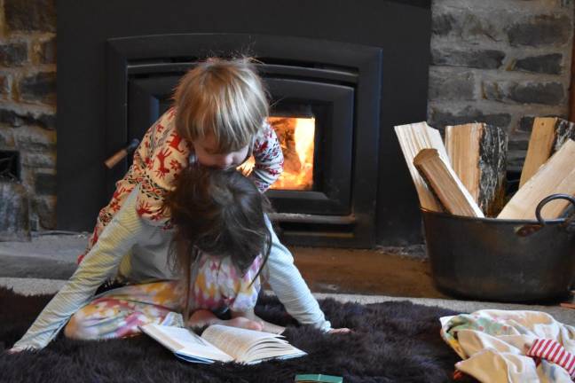 Kai, 9, maintains focus on her library book while Dion, 3, looks on, simultaneously riding his sister like a horsey.