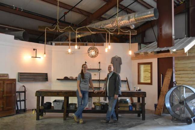 Lauren and Dale Van Pamelen. Dale picked up the old machine shop table for $20. This will be the retail section, holding folded hats and t-shirts. Above them hangs a 300-year-old barn beam that he found on Facebook Markeplace.