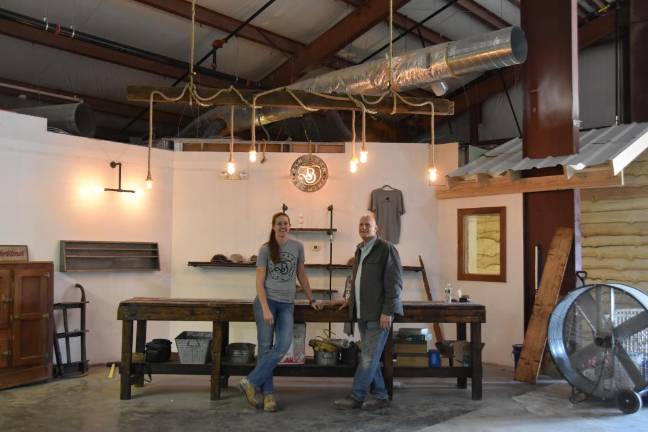 Gleefully DIY Lauren and Dale Van Pamelen. Dale picked up the old machine shop table for $20. This will be the retail section, holding folded hats and t-shirts. Above them hangs a 300-year-old barn beam that he found on Facebook Markeplace.