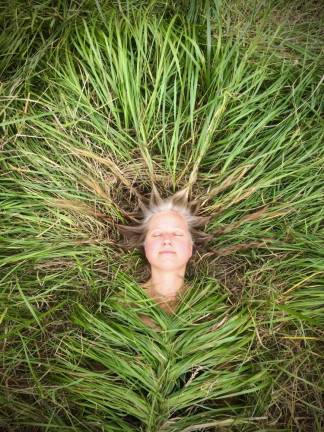 In<i> Grass Cocoon </i>(2018), a smiling woman is wrapped in long green grass, her body snugly tucked into the ground and her hair woven into the meadow that engulfs her.
